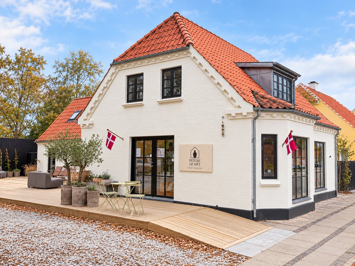 House of Art: det hvide hus med rødt tegltag, danske flag og en træterrasse med oliventræer foran indgangen